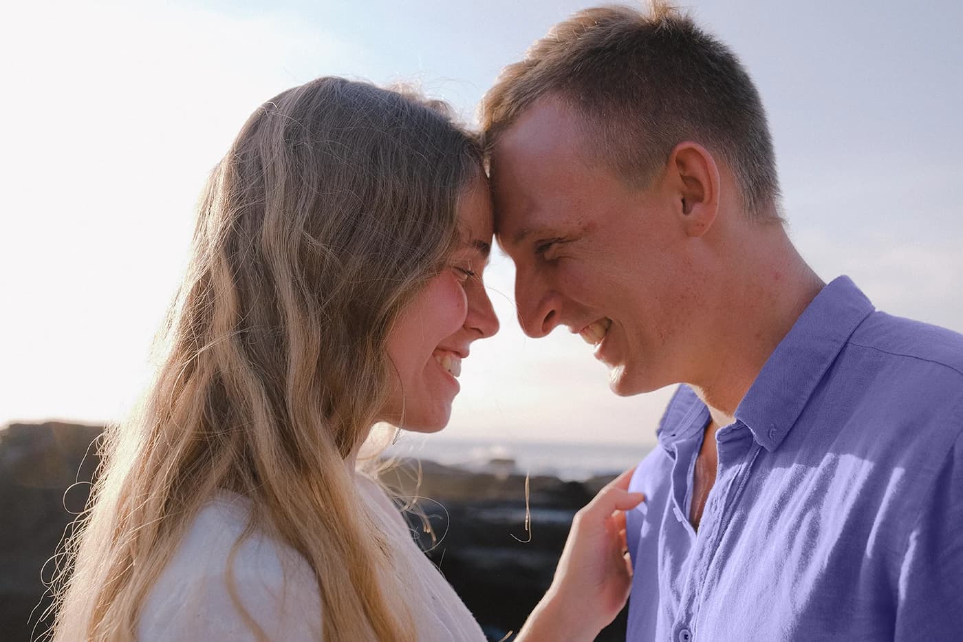 A close up photo of a couple smiling outside in sunlight