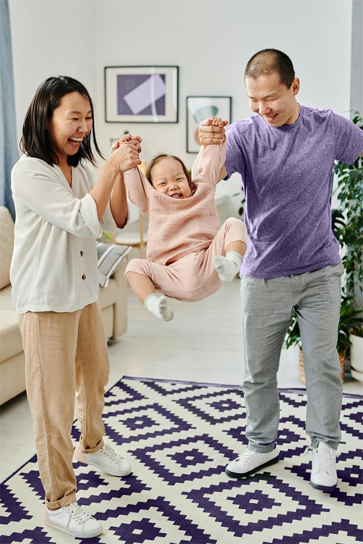 a smiling young asian couple holding up their child
